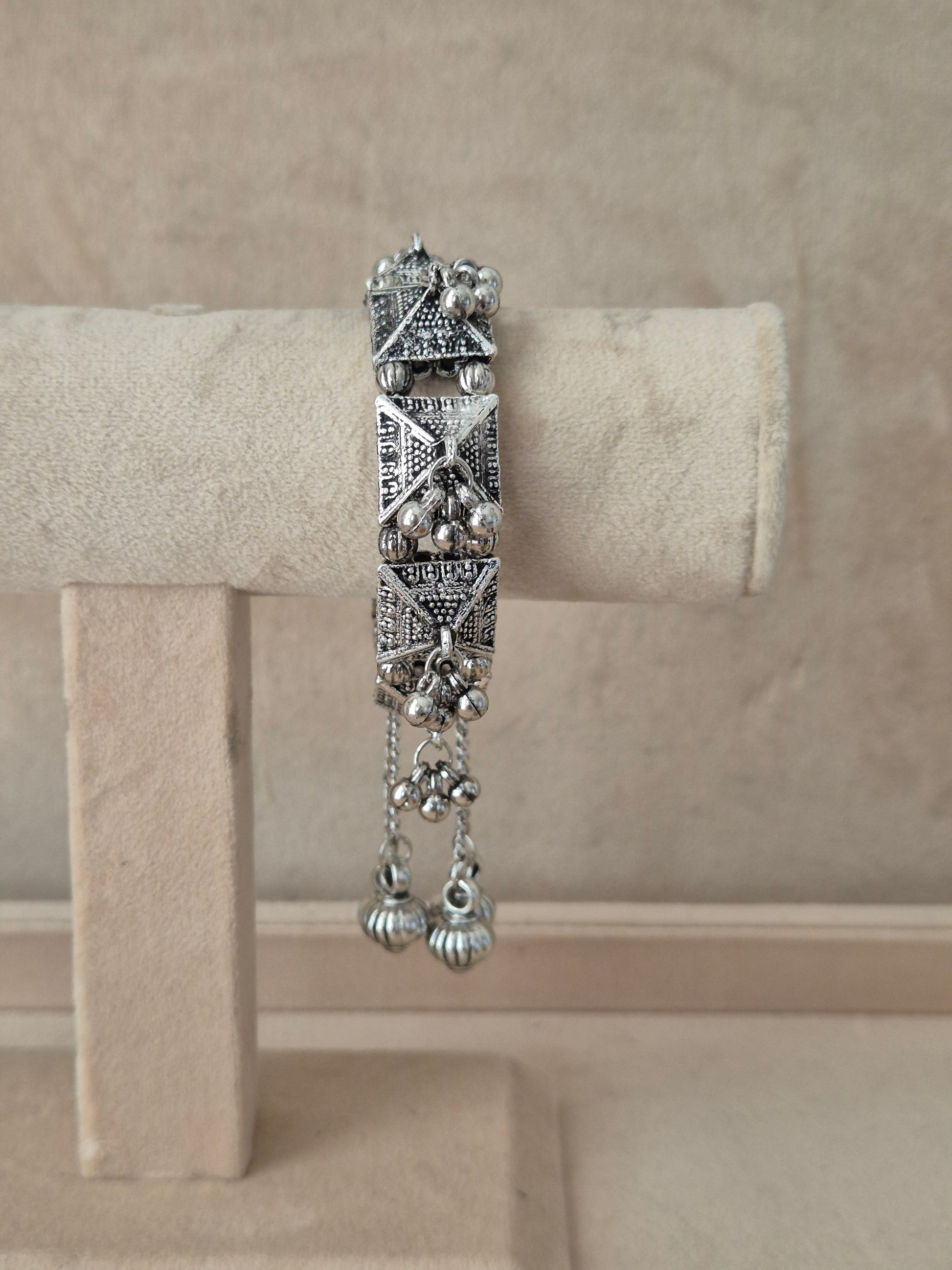 Oxidized silver Alaknanda bangle bracelet with intricate geometric patterns, textured pyramid elements, and dangling ghungroo metallic beads by naitri.in