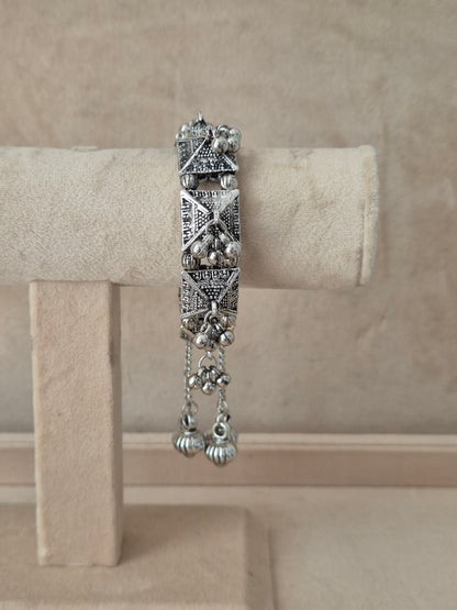 Oxidized silver Alaknanda bangle bracelet with intricate geometric patterns, textured pyramid elements, and dangling ghungroo metallic beads by naitri.in