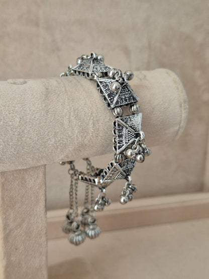 Bohemian-style silver-plated statement cuff bracelet featuring diamond cutout filigree textures and hanging bell charms on a luxury jewelry display stand by naitri.in