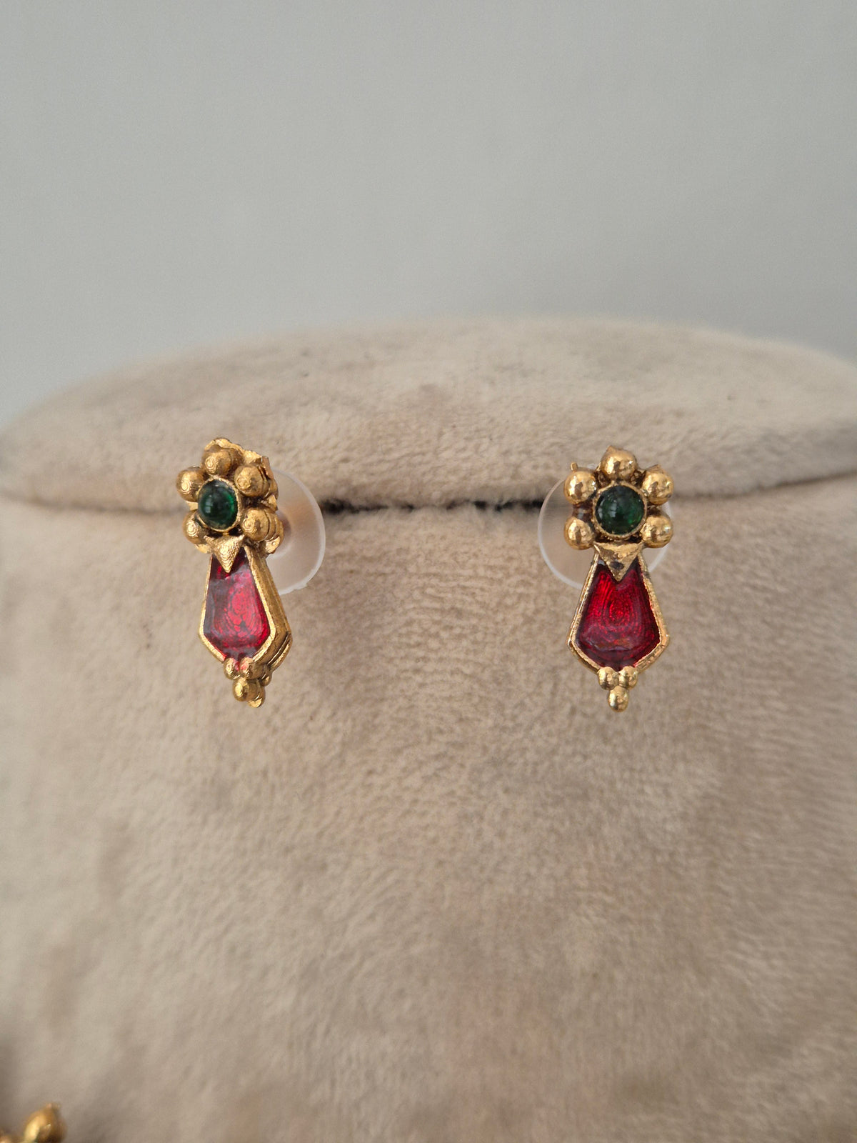 A pair of gold-toned stud earrings with green oval stones at the top and red teardrop-shaped stones below, by naitri.in