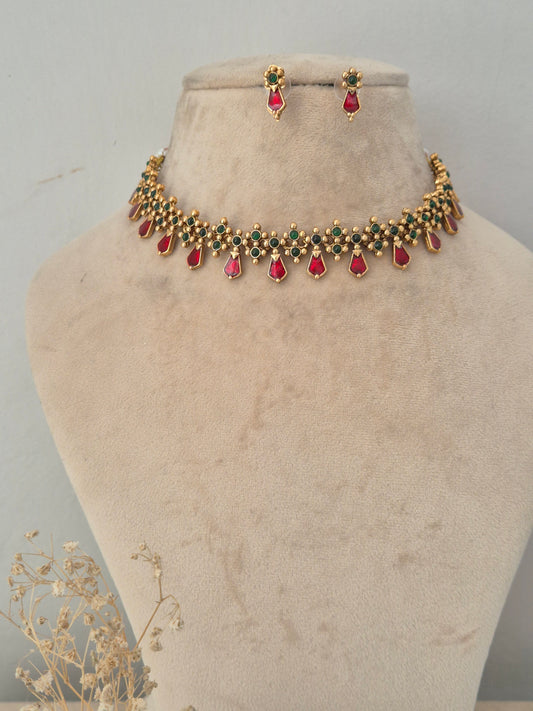 Traditional gold choker necklace featuring intricate green and red stone work with tear-drop ruby stone pendants with matching small stud earrings by naitri.in
