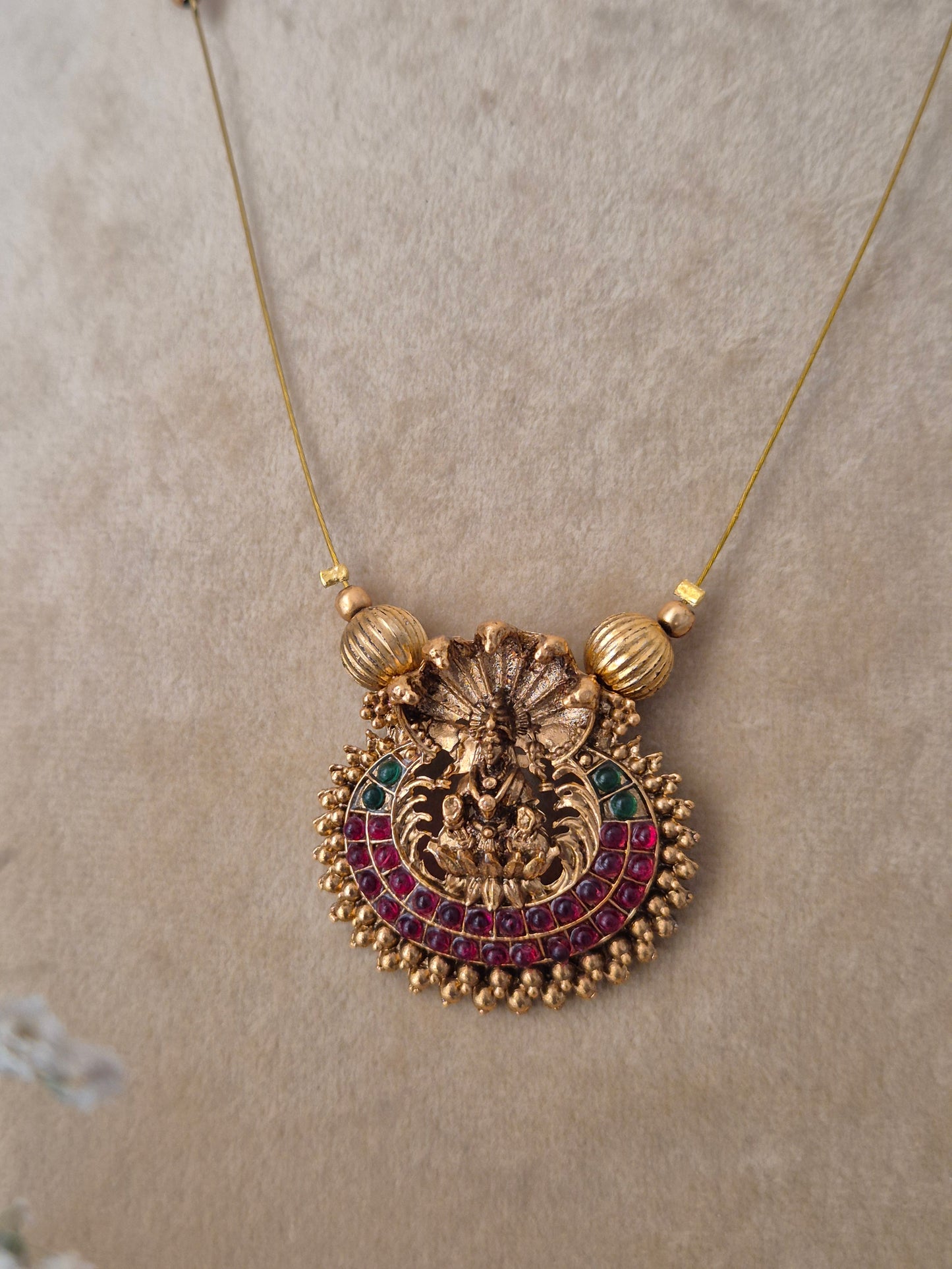 Minimalist invisible chain necklace with a textured gold-polished pendant and red-green stone embellishments, paired with matching red and gold earrings for a modern Indian aesthetic by naitri.in