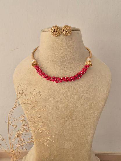 Ambika Red Beaded Choker Set displayed on a beige mannequin, featuring a tightly wound multi-strand red bead collar complemented by matching traditional gold stud earrings by Naitri.in