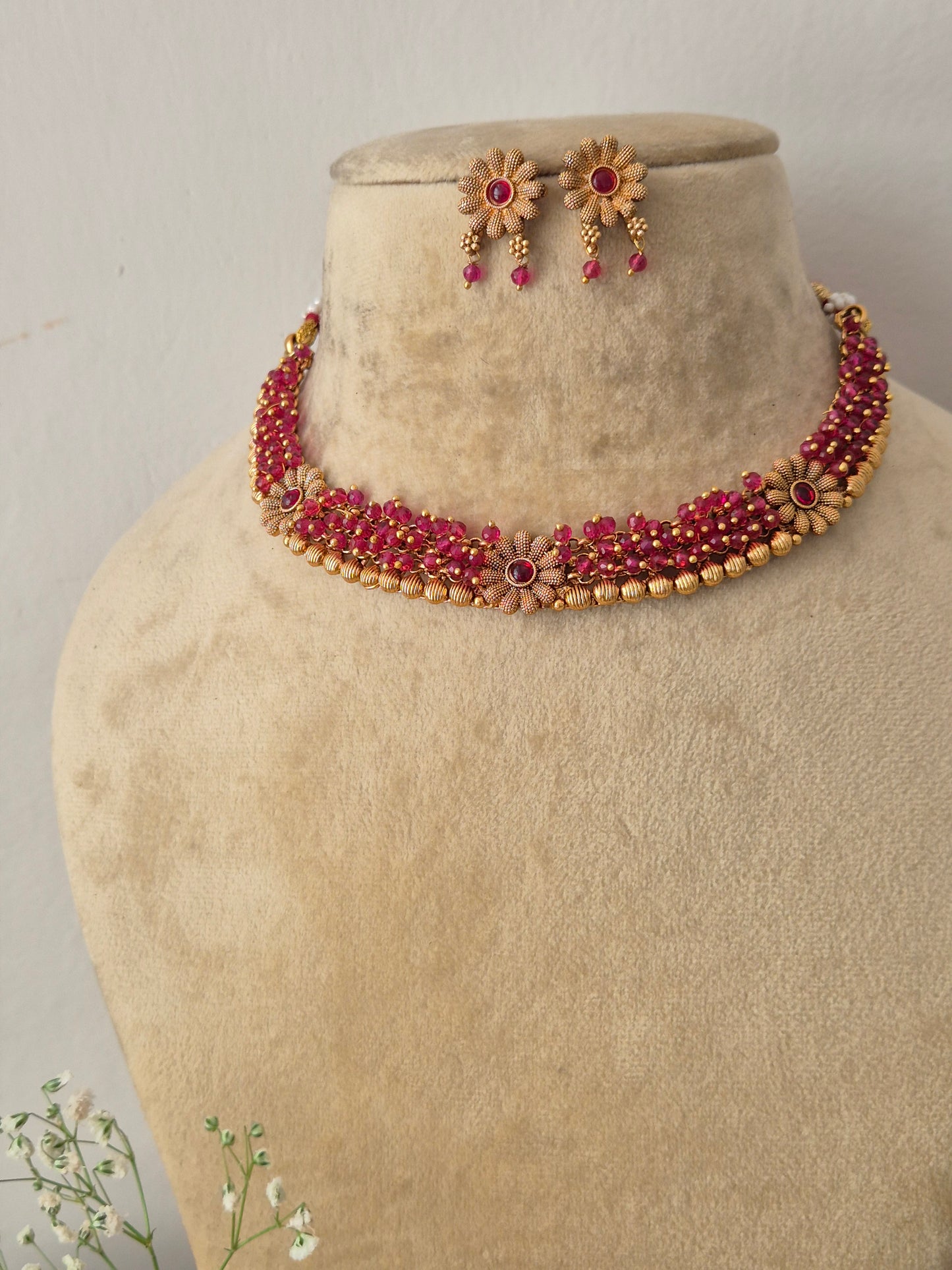 Gold-plated choker necklace with pink-red floral gemstones and matching earrings by naitri.in
