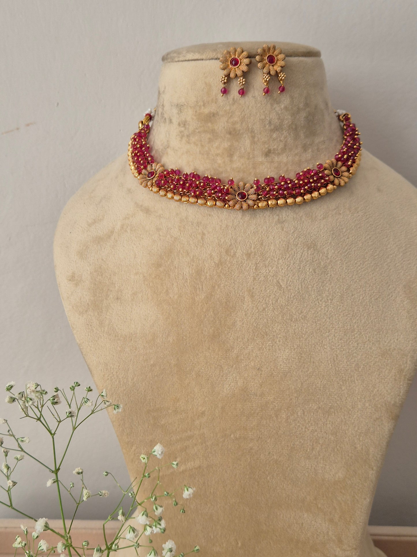 A gold-plated multi-strand choker necklace featuring pinkish-red ruby stones and intricate floral accents with matching hanging stud earrings by naitri.in