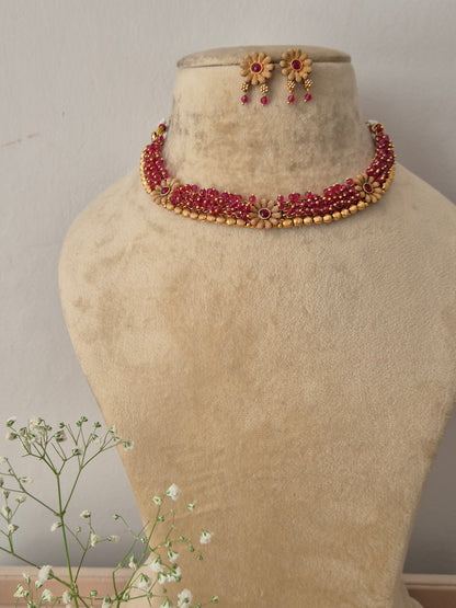A gold-plated multi-strand choker necklace featuring pinkish-red ruby stones and intricate floral accents with matching hanging stud earrings by naitri.in