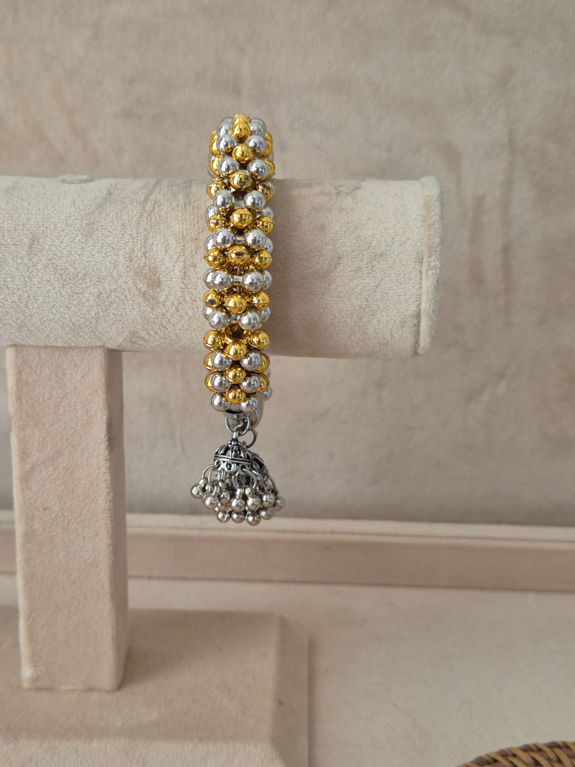 Statement gold and silver-plated festive Kada bangle featuring intricate rows of metallic beads and hanging bell charms by naitri.in