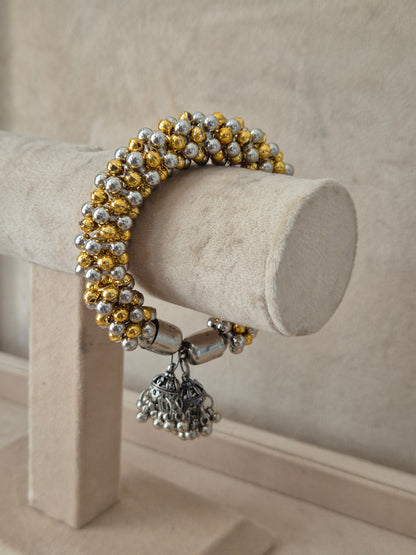 Dual-toned gold and silver Amukta bangle with dangling oxidized silver jhumka Elegant dual-tone ethnic bracelet with traditional festive details by naitri.in