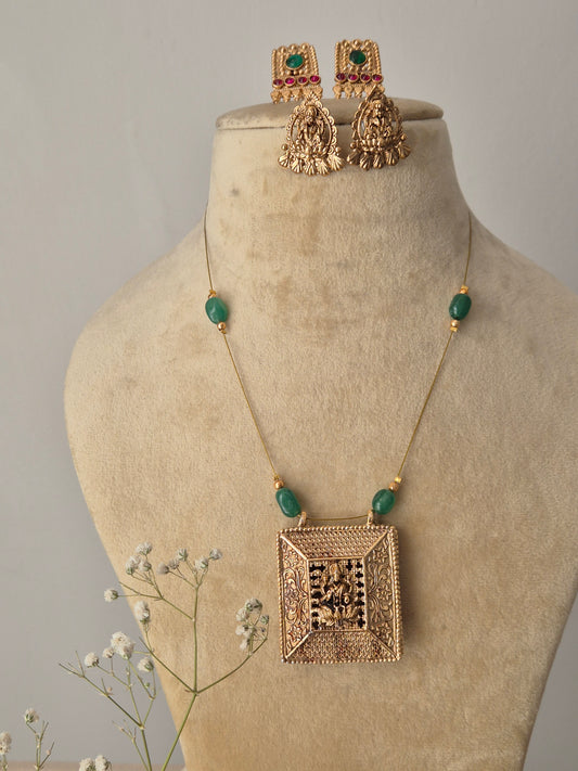 Handcrafted invisible chain necklace with a textured gold square pendant and green stone accents, paired with ornate gold and red stone earrings for a modern Indian look by naitri.in