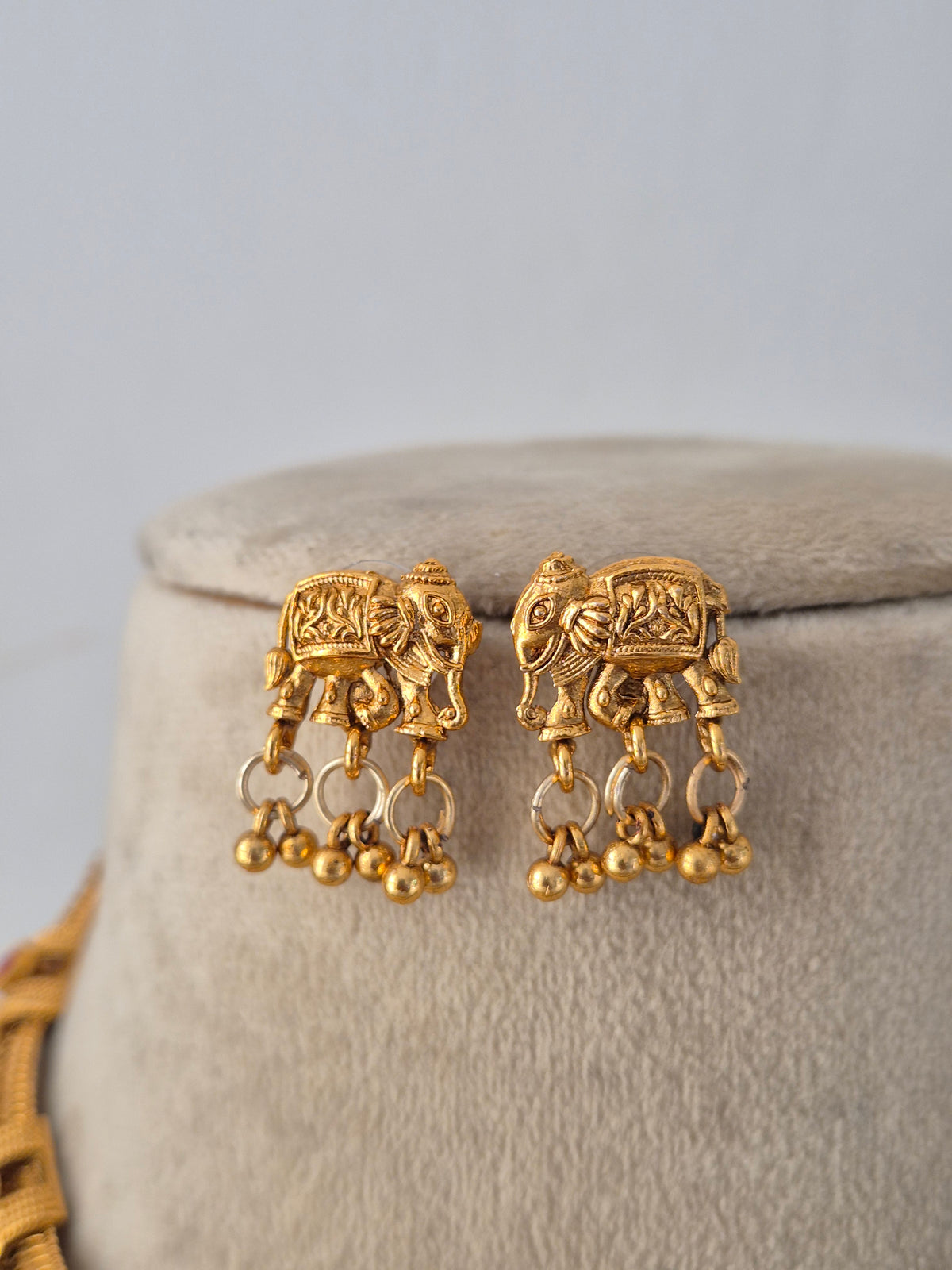the handcrafted Mannu Necklace Set displayed on a neutral mannequin bust. The brass alloy choker is detailed with traditional ethnic motifs and vibrant gemstone accents. A pair of matching jhumka earrings rests neatly above the necklace, completing the traditional set by Naitri.in