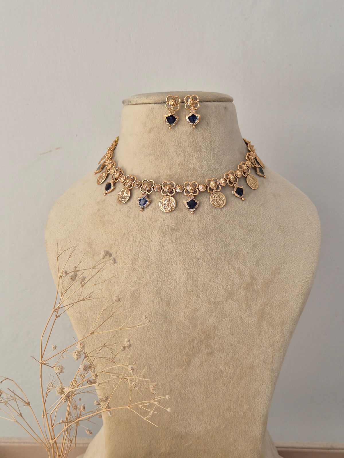 Anushka Gold Charm Choker Set displayed on a neutral beige mannequin, featuring a delicate gold-toned chain accented with dangling circular motifs, dark blue gemstone insets, and matching stud earrings by Naitri.in
