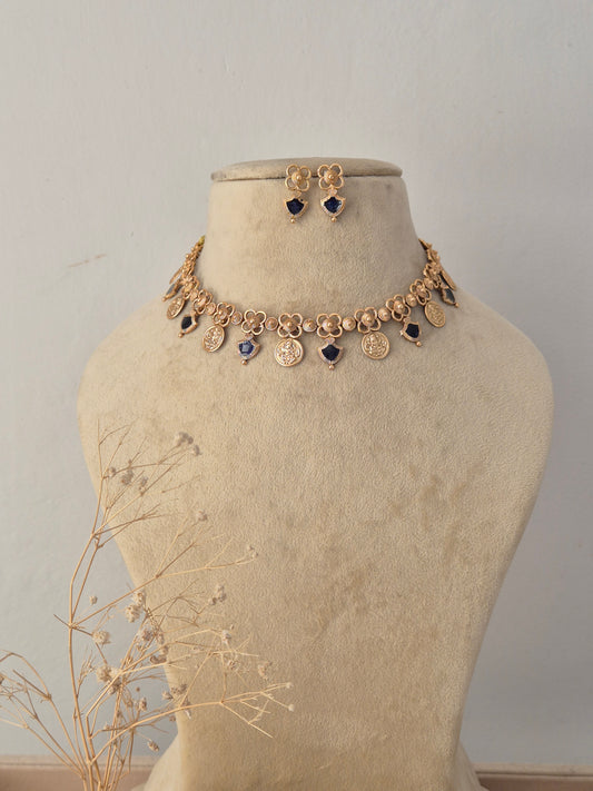 Anushka Gold Charm Choker Set displayed on a neutral beige mannequin, featuring a delicate gold-toned chain accented with dangling circular motifs, dark blue gemstone insets, and matching stud earrings by Naitri.in