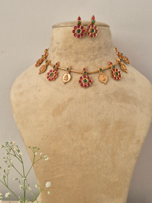 A gold-plated choker necklace featuring alternating red and green gemstone drops and traditional coin motifs  with matching floral-themed hanging earrings by naitri.in