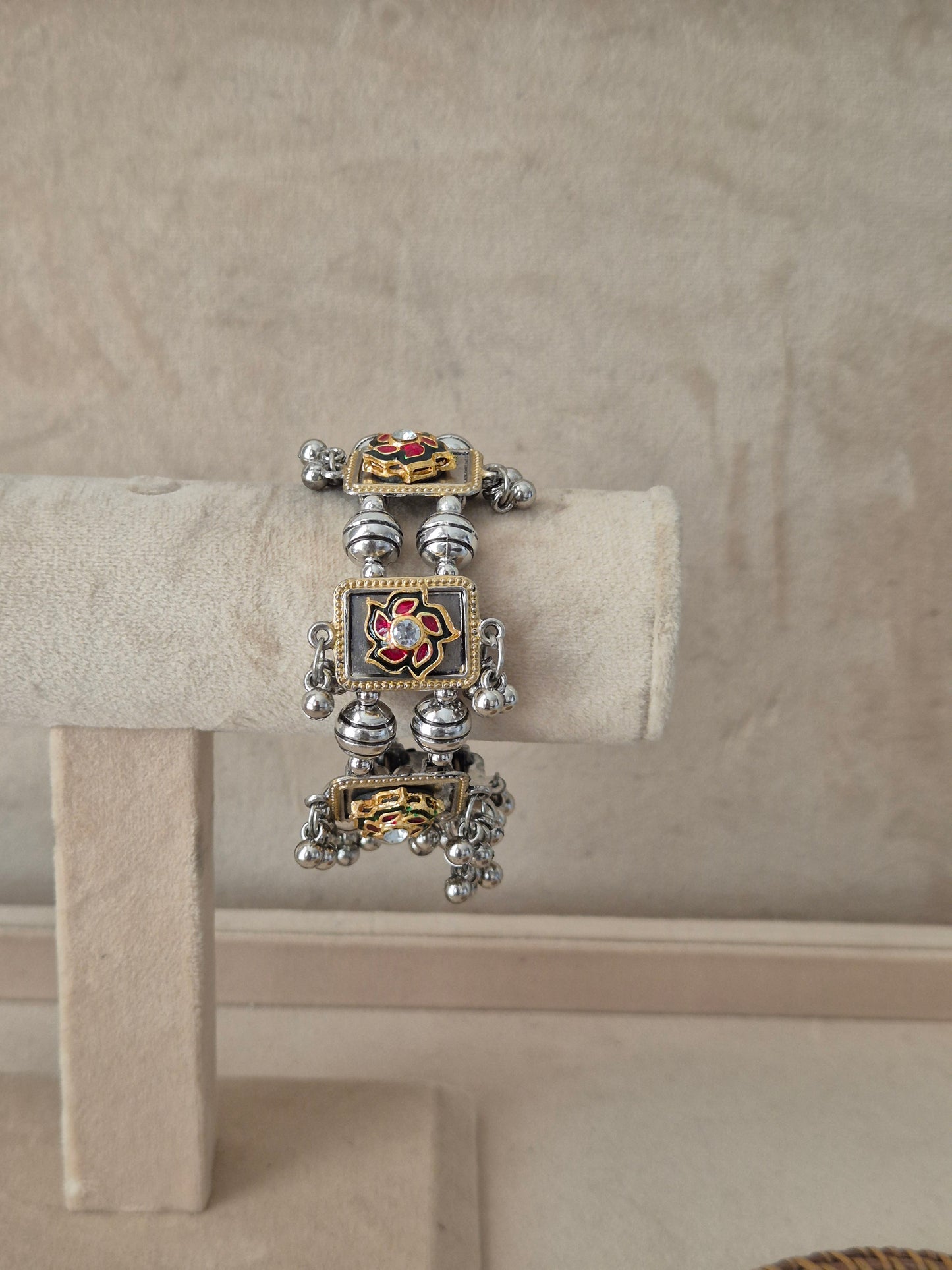 Dual-tone Apeksha bangle bracelet featuring a central square charm with a red and green floral enamel design and clear crystal center, flanked by oxidized silver beads and dangling metallic ghungroo balls by naitri.in