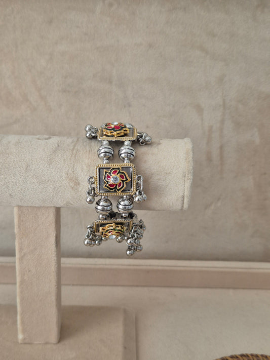 Dual-tone Apeksha bangle bracelet featuring a central square charm with a red and green floral enamel design and clear crystal center, flanked by oxidized silver beads and dangling metallic ghungroo balls by naitri.in