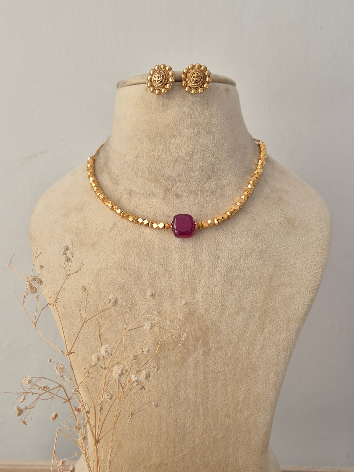 Traditional gold-plated choker necklace set featuring a vibrant pink center stone, displayed on a mannequin with matching stud earrings by Naitri.in