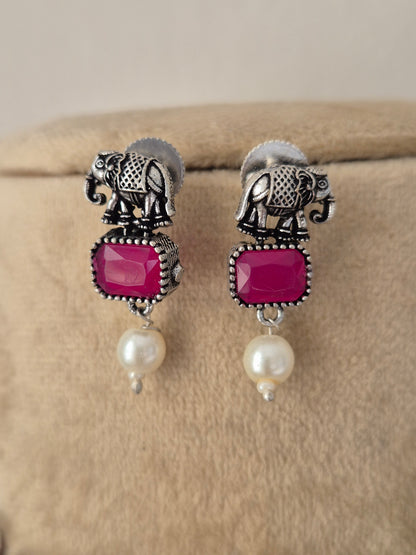 A pair of silver-toned drop earrings featuring elephant motifs, rectangular magenta-pink gemstones, and dangling white pearls, by naitri.in