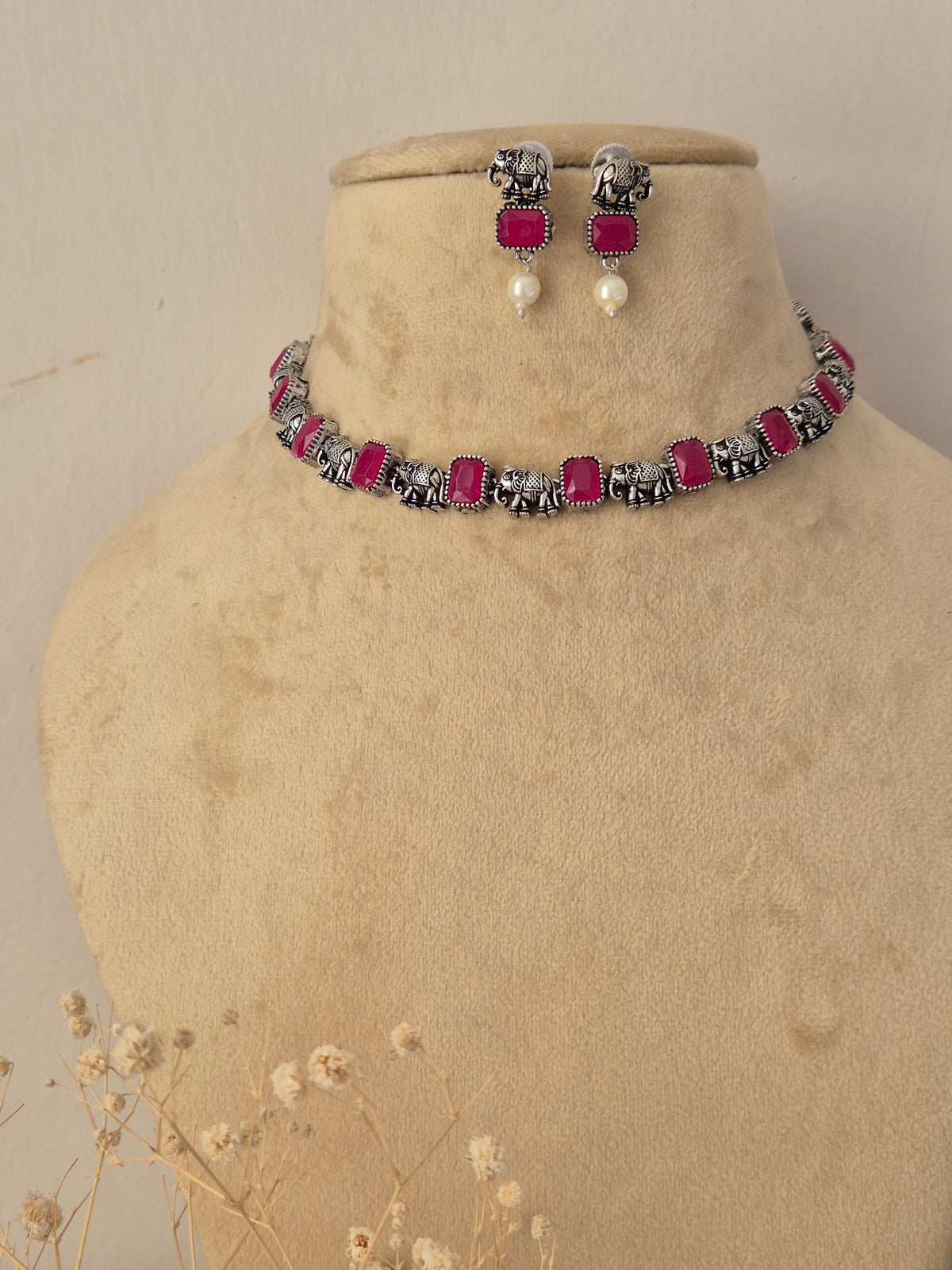 A silver-toned jewelry set featuring a choker necklace and matching drop earrings with rectangular magenta-pink stones and white pearl drops, by naitri.in