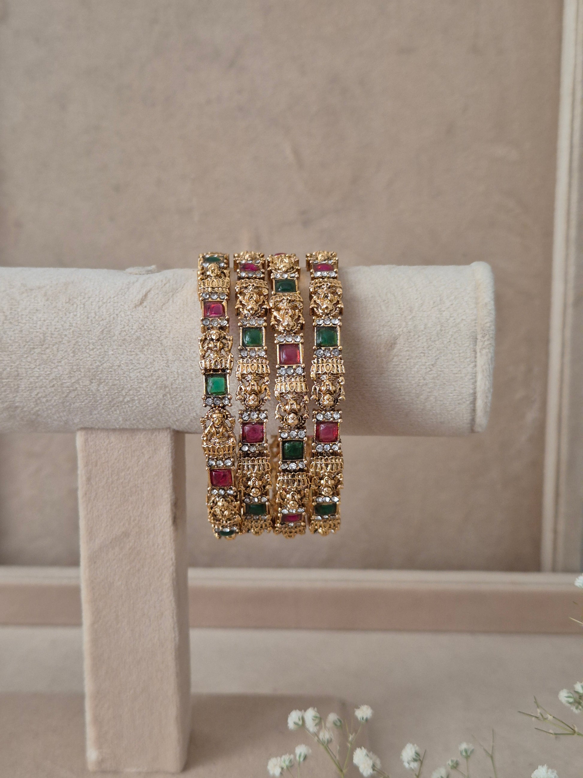 A set of four gold-plated Ashika bangles featuring intricate metalwork engraving and alternating square-cut red and green gemstones by naitri.in