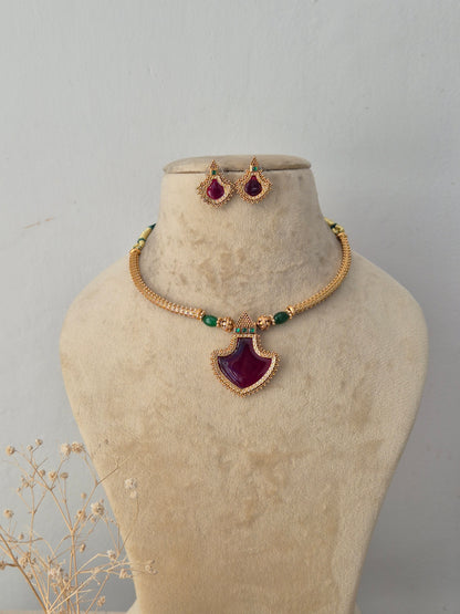 Astami gold-toned ethnic necklace set featuring a striking teardrop ruby-colored pendant, green beaded accents, and matching teardrop stud earrings by Naitri.in