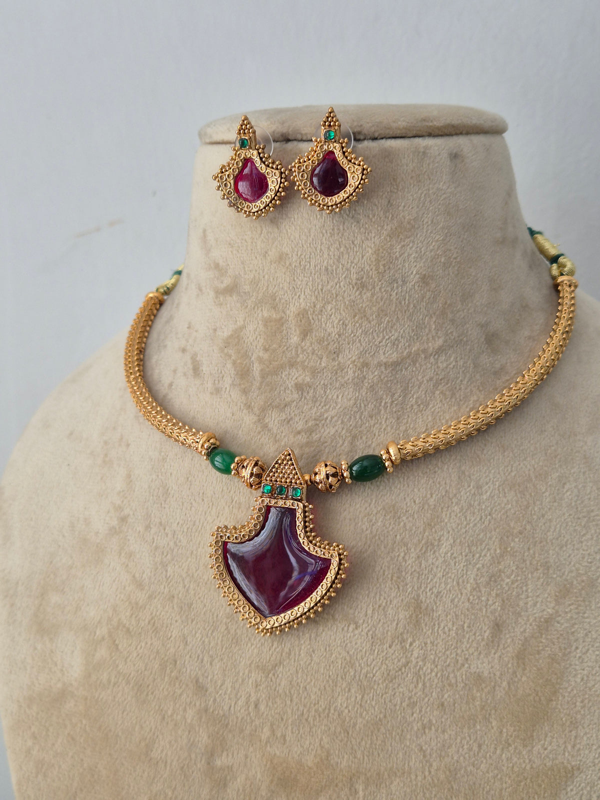 Handcrafted brass alloy ethnic necklace featuring a bold central red stone, delicate green bead embellishments, and matching teardrop stud earrings by Naitri.in