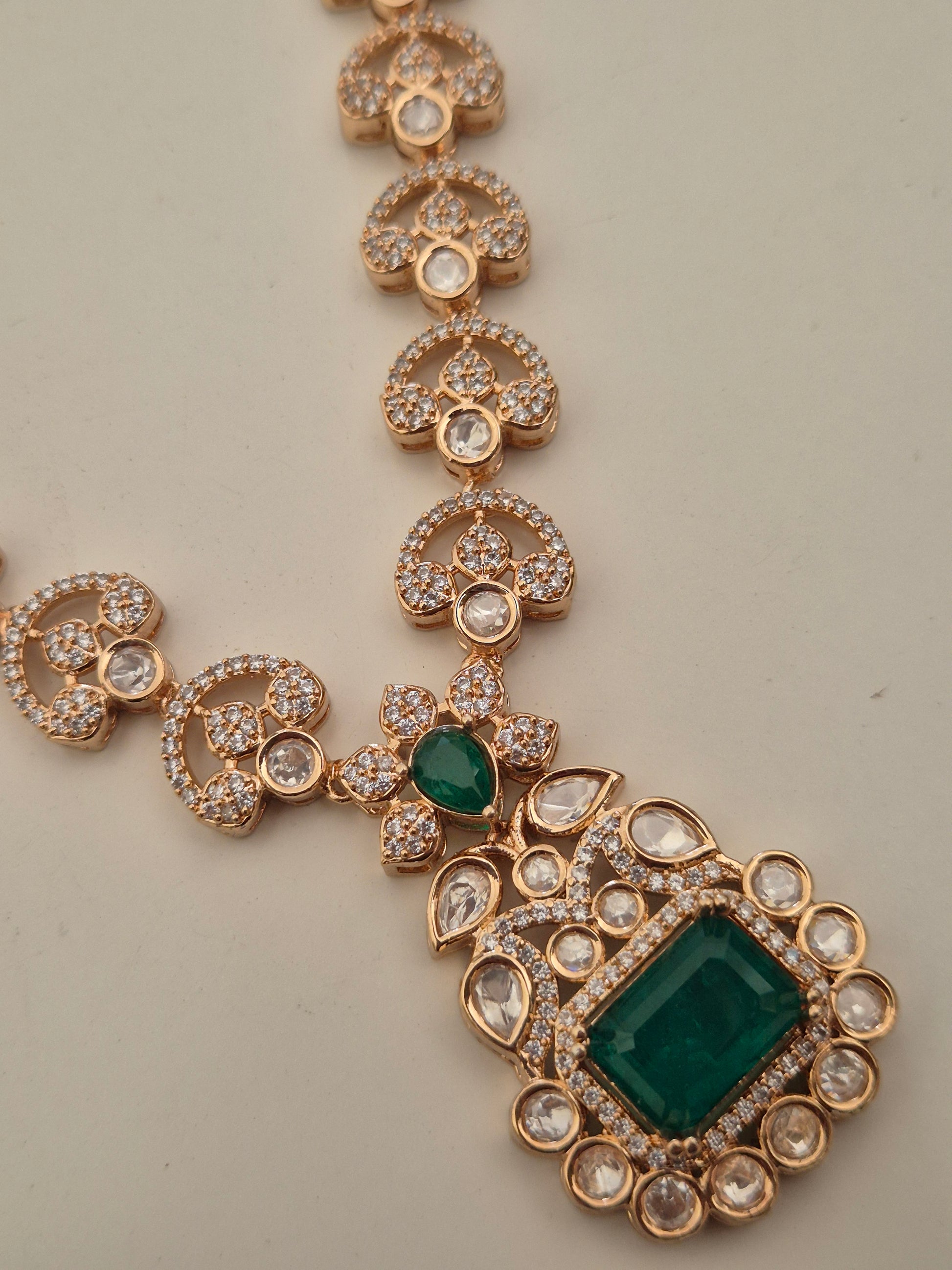 Alloy necklace set featuring floral crystal patterns and a central emerald-cut green stone pendant by naitri.in