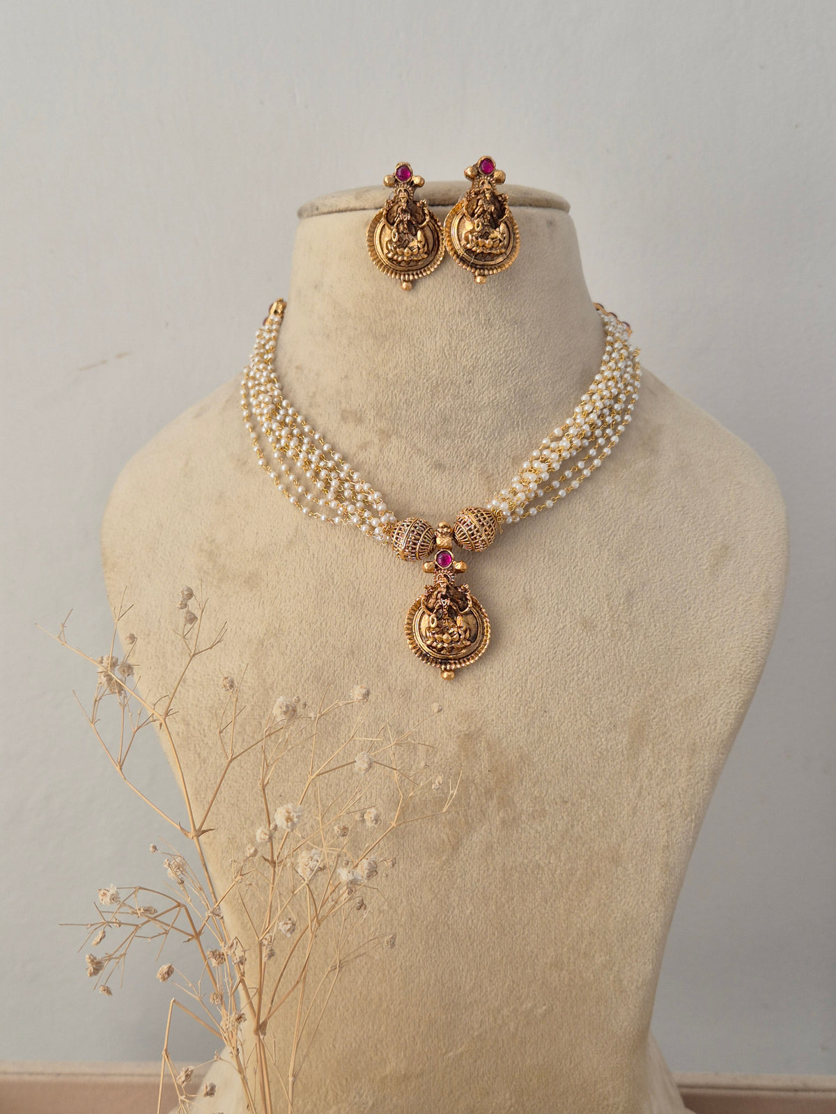 Traditional gold-plated multi-layer bead necklace set with a central temple pendant, displayed on a mannequin with matching jhumka earrings by Naitri.in