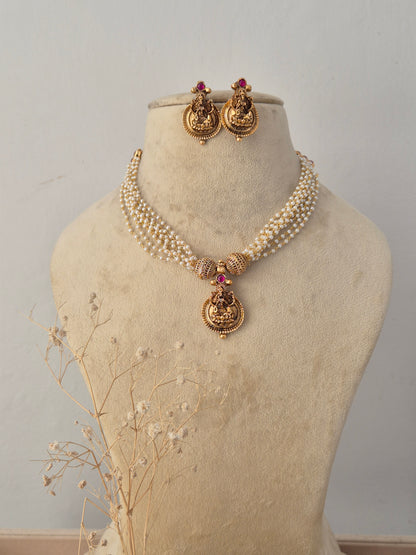 Traditional gold-plated multi-layer bead necklace set with a central temple pendant, displayed on a mannequin with matching jhumka earrings by Naitri.in