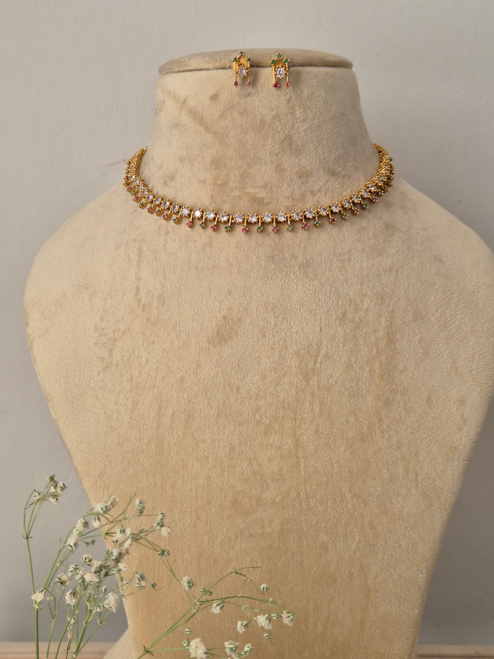 Gold-plated single-strand choker necklace featuring alternating clear crystals and ruby-red stones, with matching earrings by naitri.in