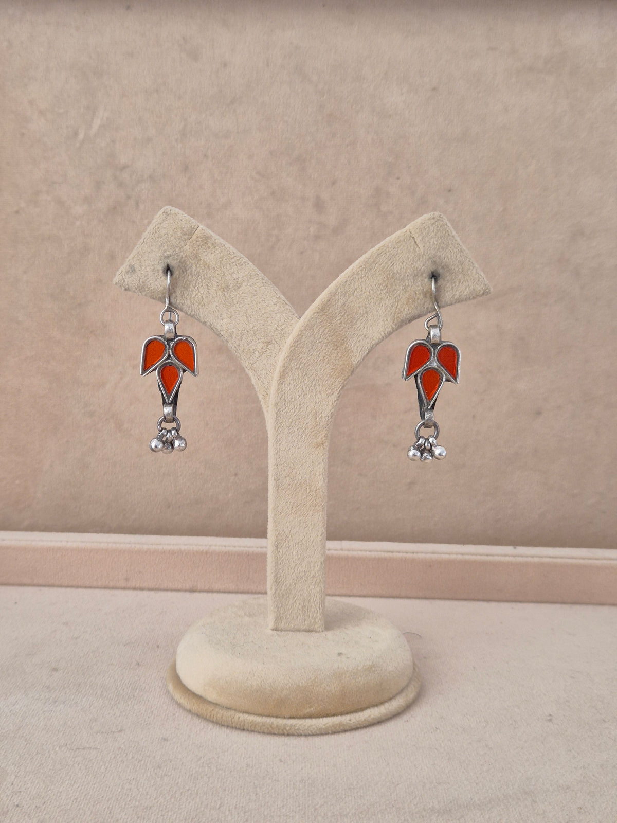 A pair of silver-toned dangle earrings with red glass in a leaf design with small silver beads by naitri.in