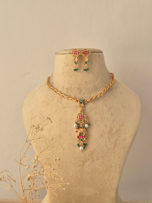 Bansari Gold Pendant Necklace Set displayed on a neutral beige mannequin, featuring a delicate twisted gold chain paired with an intricate pendant accented with colorful gemstones and hanging pearl beads, along with matching studs by Naitri.in