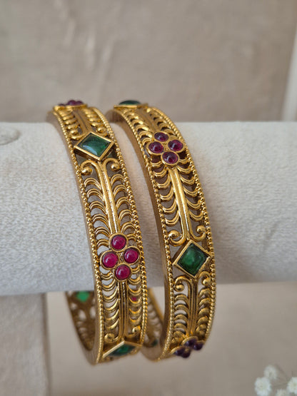 Intricate gold-plated ethnic bangles with red and green gemstone accents by naitri.in