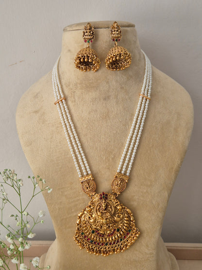 Elegant traditional gold-toned ethnic jewelry set featuring a detailed divine motif pendant and pearl layers, Gold-plated temple pendant necklace with multi-strand pearl chain and matching jhumka earrings by naitri.in