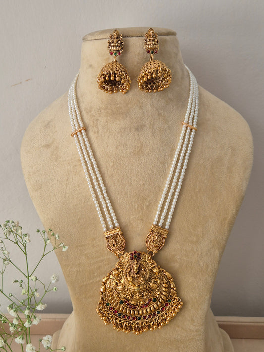 Elegant traditional gold-toned ethnic jewelry set featuring a detailed divine motif pendant and pearl layers, Gold-plated temple pendant necklace with multi-strand pearl chain and matching jhumka earrings by naitri.in