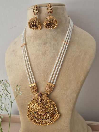 A traditional gold-plated temple jewelry pendant featuring an intricate goddess design, suspended from a multi-strand white pearl chain with  matching jhumka earrings by naitri.in