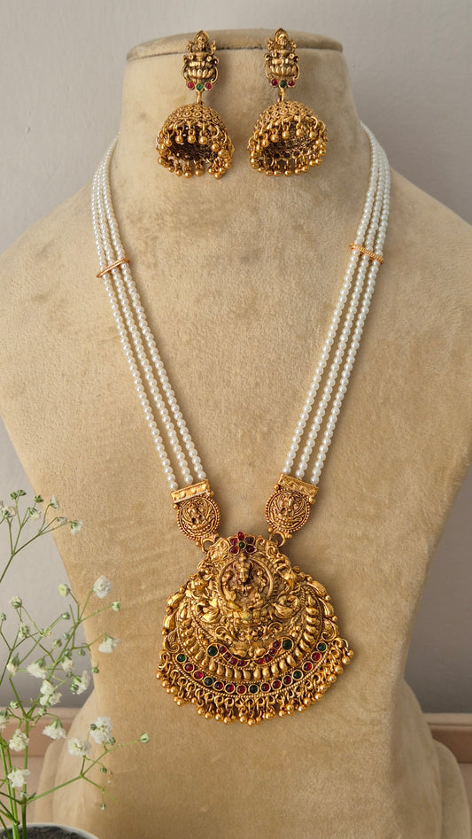 A traditional gold-plated temple jewelry pendant featuring an intricate goddess design, suspended from a multi-strand white pearl chain with  matching jhumka earrings by naitri.in