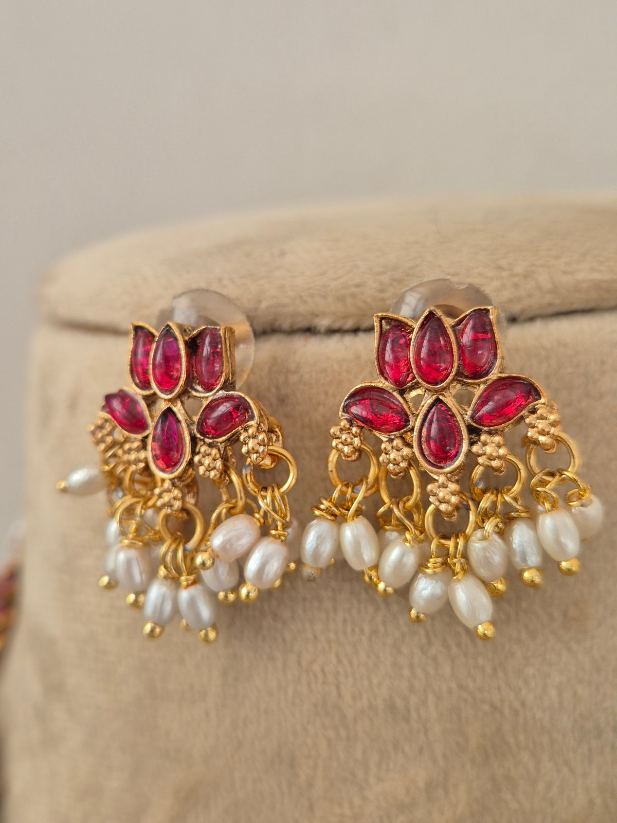 A pair of gold-plated Indian jhumka earrings with red stone accents and white pearl-like beads, by naitri.in