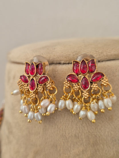 A pair of gold-plated Indian jhumka earrings with red stone accents and white pearl-like beads, by naitri.in
