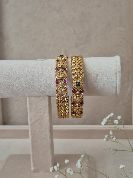 Set of 2 Bhaghirathi gold bangles by Naitri featuring intricate traditional floral engravings, accented with ruby-red and emerald-green gemstones by naitri.in