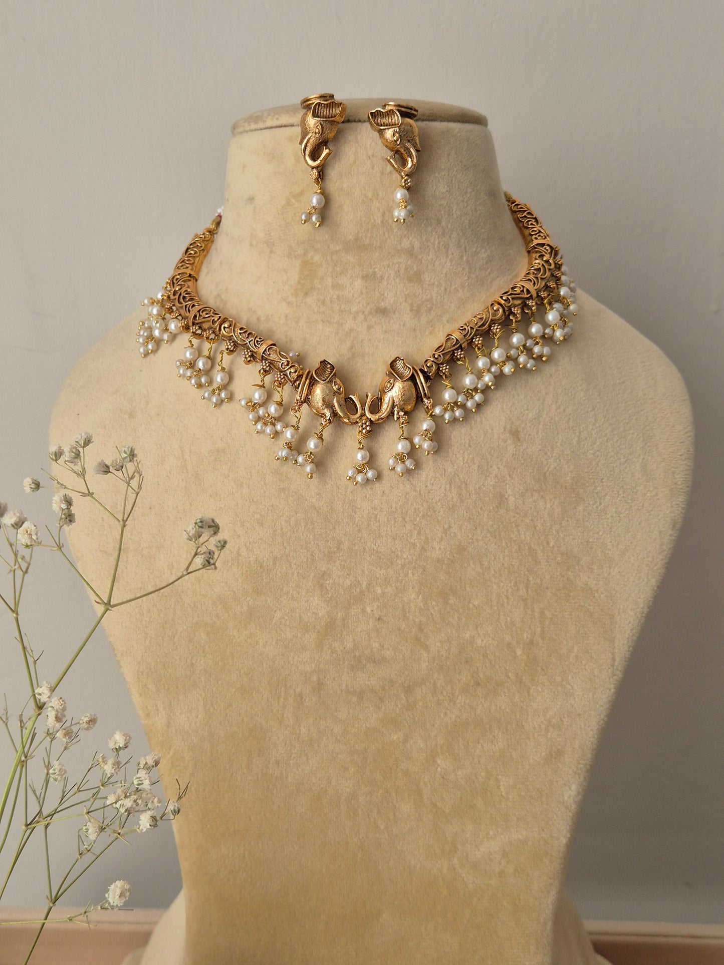 Bhagrati necklace set featuring an intricate gold choker adorned with white pearl drops and matching gold-plated drop earrings by naitri.in
