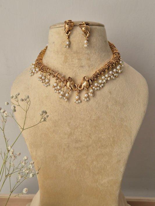 Bhagrati necklace set featuring an intricate gold choker adorned with white pearl drops and matching gold-plated drop earrings by naitri.in