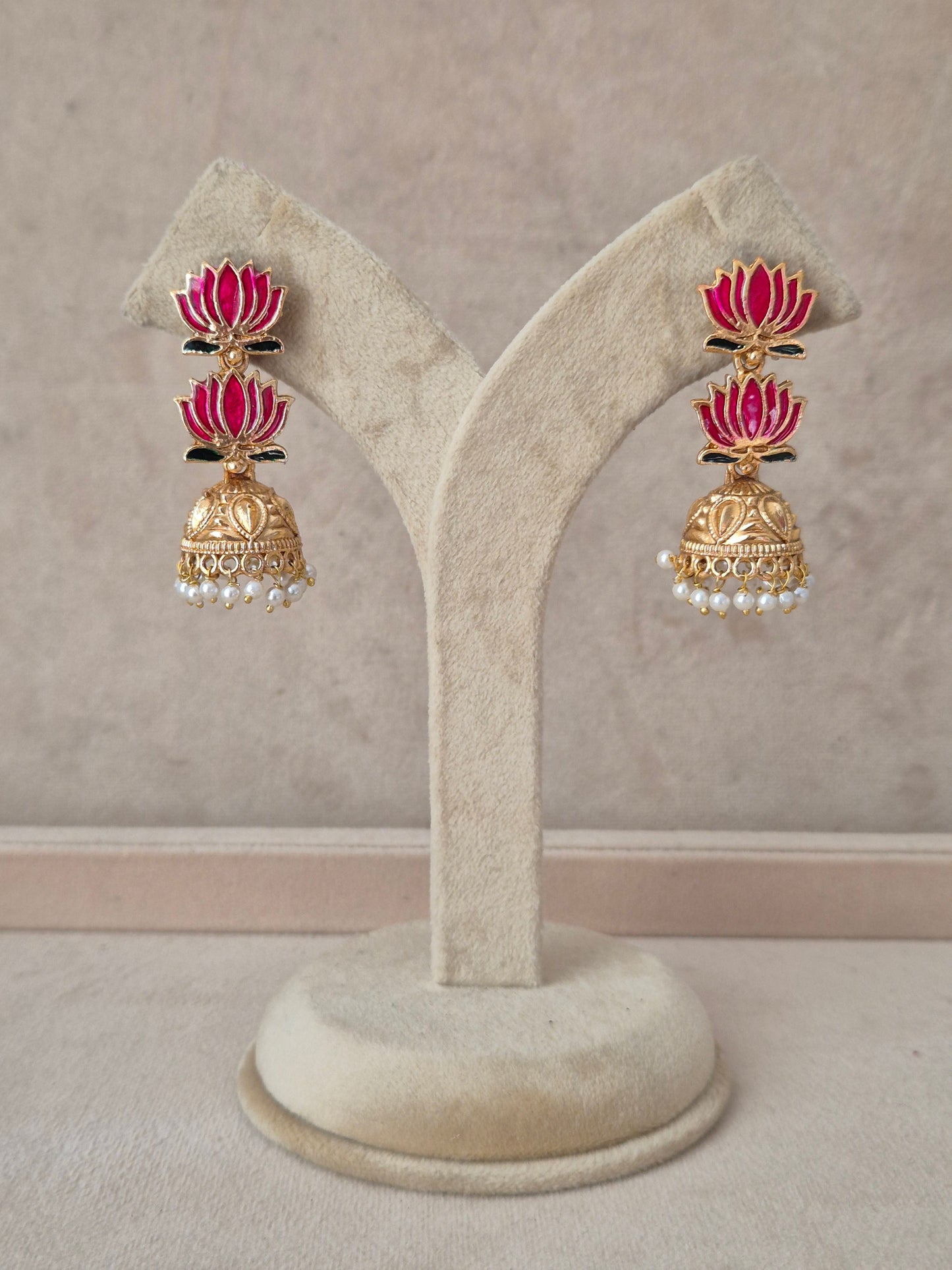 A pair of gold-toned jhumka earrings with pink and red floral motifs, black enamel details, and small white pearl-like accents, by naitri.in