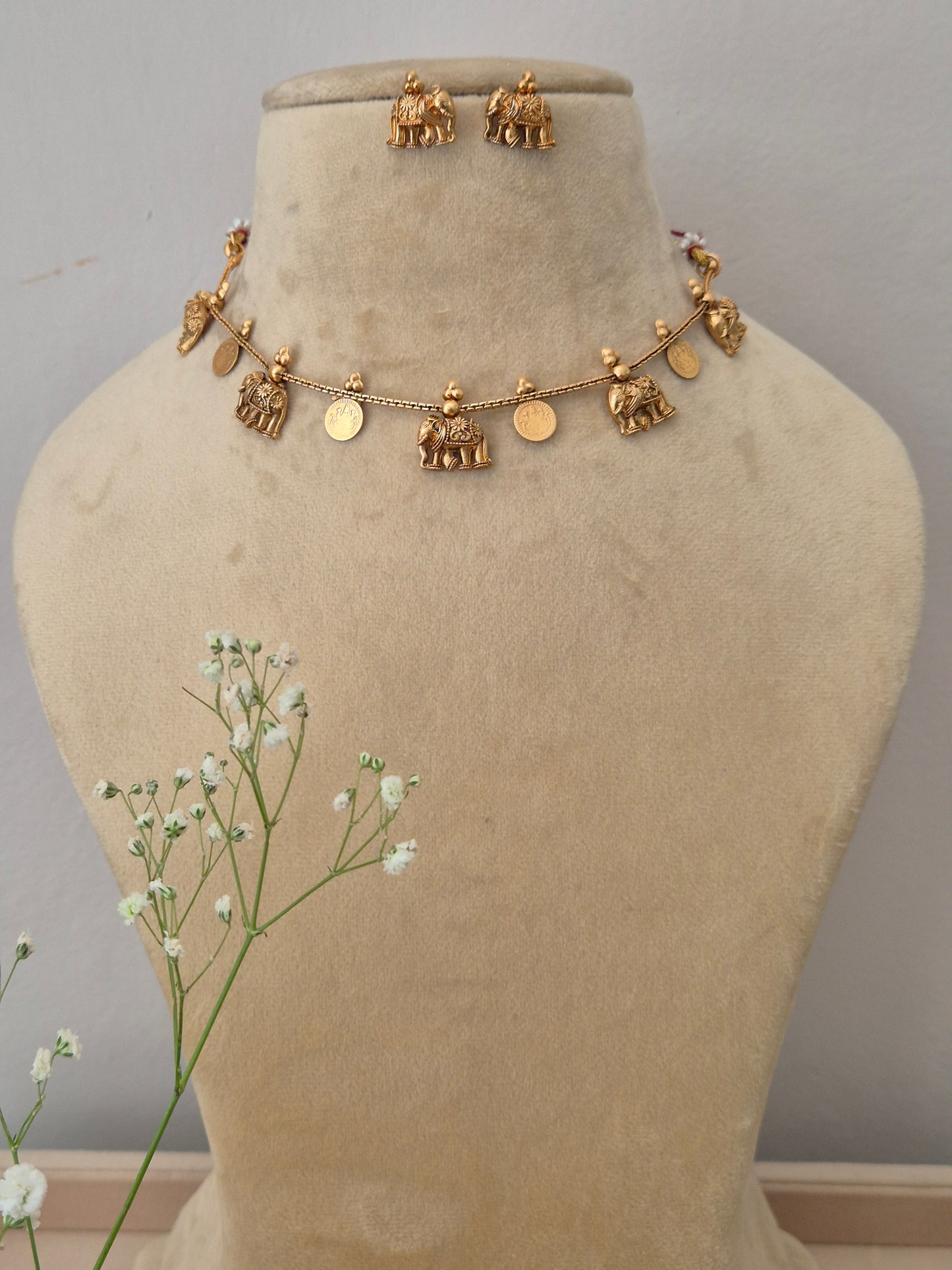  An elegant gold-plated choker necklace featuring traditional coin and temple-style dangling charms, displayed with matching jhumka earrings by naitri.in