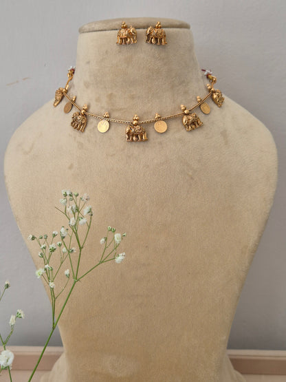  An elegant gold-plated choker necklace featuring traditional coin and temple-style dangling charms, displayed with matching jhumka earrings by naitri.in