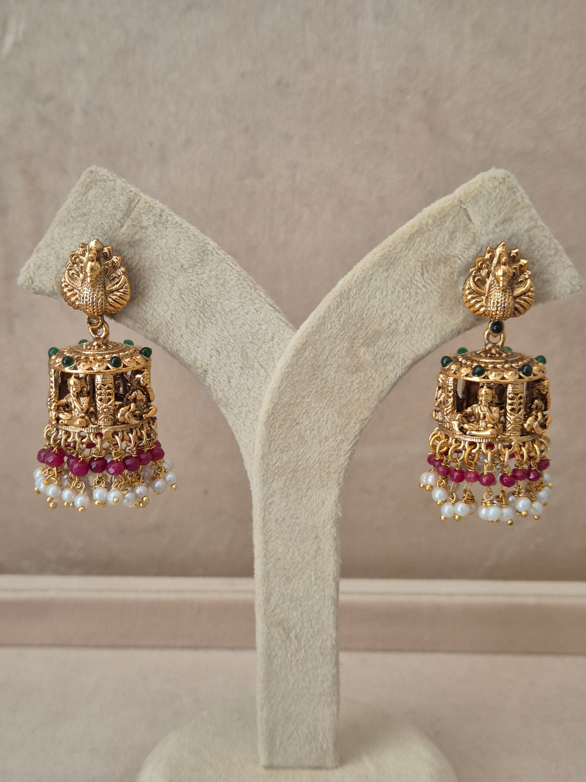 Traditional gold-toned peacock design Jhumka earrings with pink gemstones and white pearl drops by naitri.in
