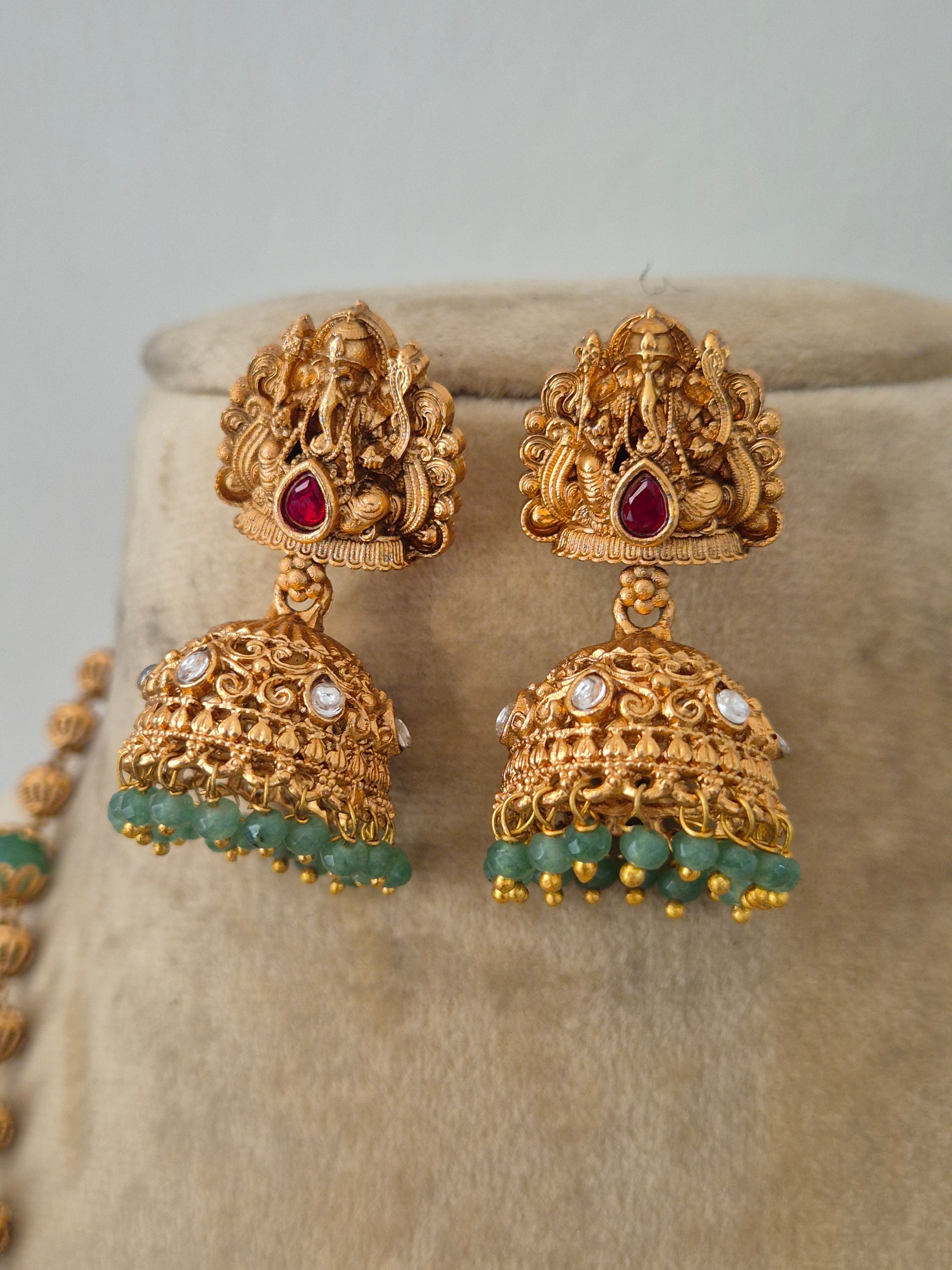 Gold-plated temple jewelry earring with a Lord Ganesha pendant, green gemstone beads, and matching jhumka earrings by naitri.in