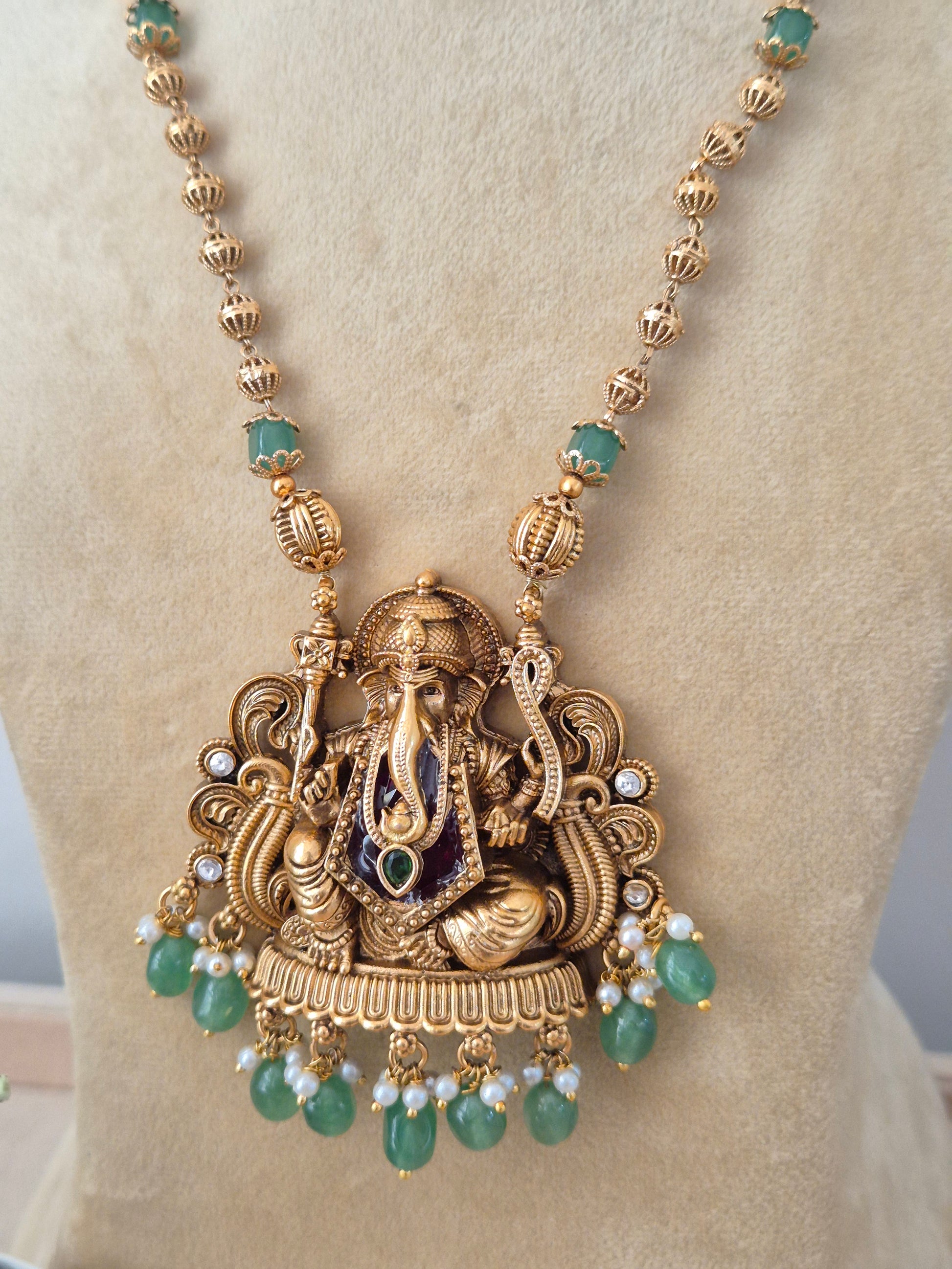 Modern Indian ethnic imitation jewelry set including a textured golden brass alloy long-chain necklace, a large detailed Ganesha motif pendant with green bead drops, by naitri.in