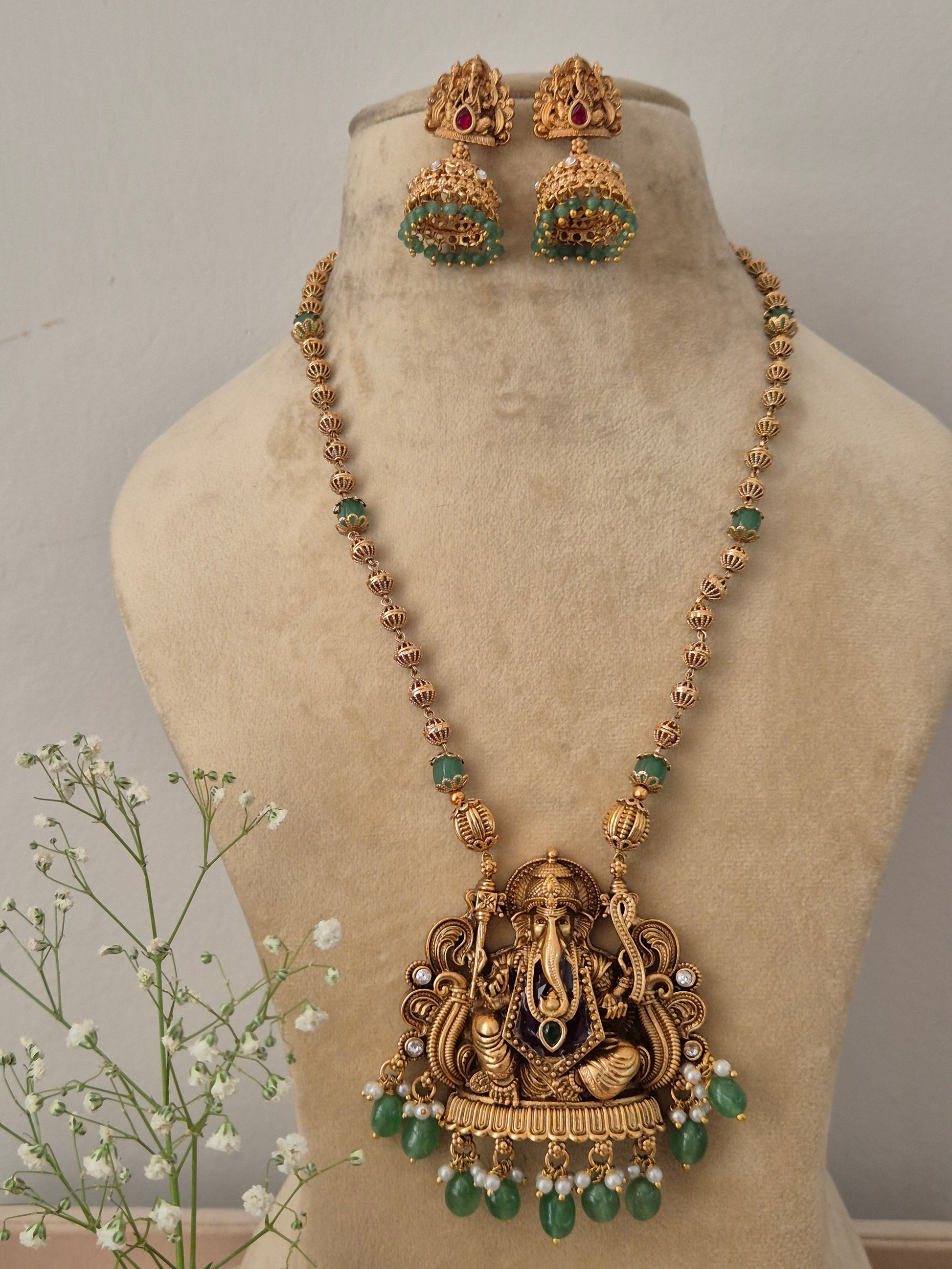 Gold-plated temple jewelry necklace with a Lord Ganesha pendant, green gemstone beads, and matching jhumka by naitri.in