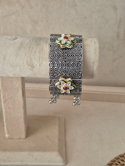 Oxidized silver Bharti bangle bracelet featuring a wide cuff design with an intricate cutout geometric filigree pattern, textured borders, and small dangling ghungroo beads, by naitri.in