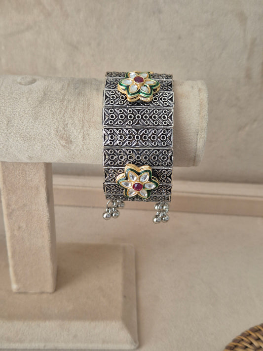 Oxidized silver Bharti bangle bracelet featuring a wide cuff design with an intricate cutout geometric filigree pattern, textured borders, and small dangling ghungroo beads, by naitri.in